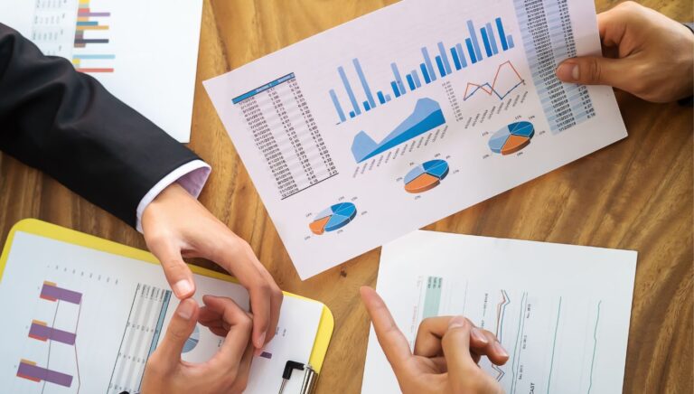 A close-up of two colleagues' hands showing paperwork with graphs and charts.