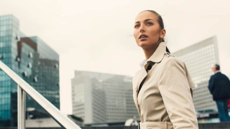 A business woman looks into the distance as she begins to climb the steps leading to towering office blocks.