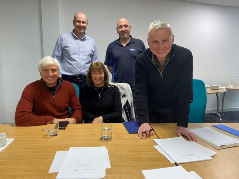 Five employees are in their office sitting and standing at a table