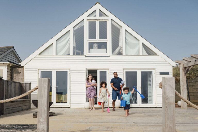 A young family emerge excitedly from their beach hut holding buckets and spades.