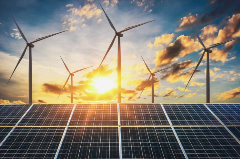 The view from below of solar panels and wind turbines against the backdrop of a cloudy sunrise.