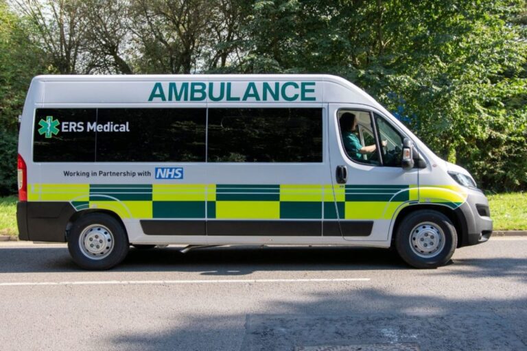 An ERS Medical ambulance is driving along a tree lined road.