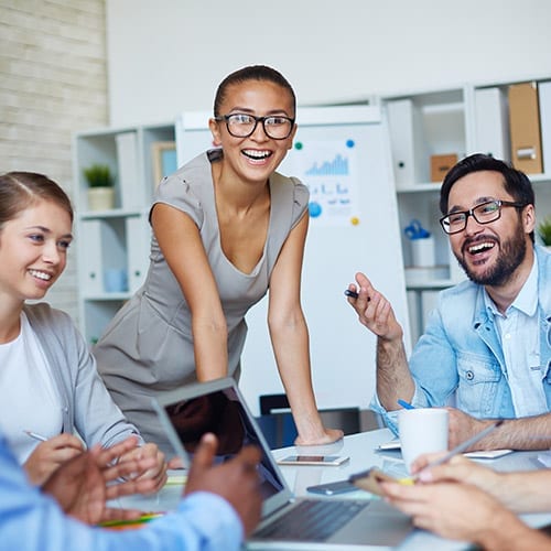 A group of office workers laugh as they have a discussion around a boardroom table.