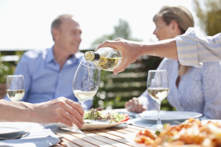 Two couples enjoy lunch and white wine while they sit in a sun drenched country garden.