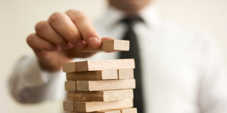 A close up image of a man's hand placing a piece on top of a wooden Jenga tower.