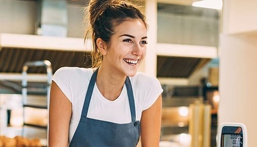 A catering business owner in an apron smiles as though she is attending to a customer.