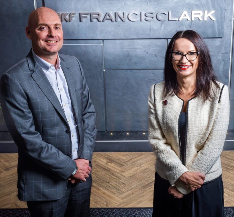 Michael Hall strikes a pose with Lucinda Coleman, in front of a slate wall and the Francis Clark sign.