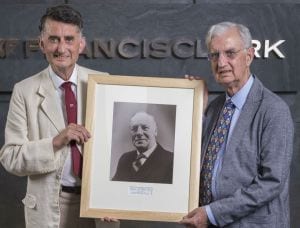 The grandsons of Francis Clark are positioned on each side of a framed photograph, standing before the sign of Francis Clark.