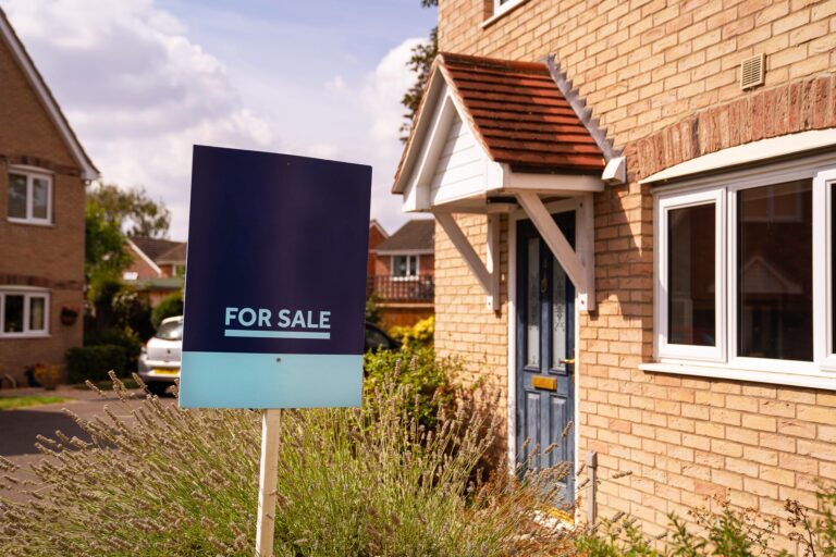 A corner house has a For Sale sign in the garden.