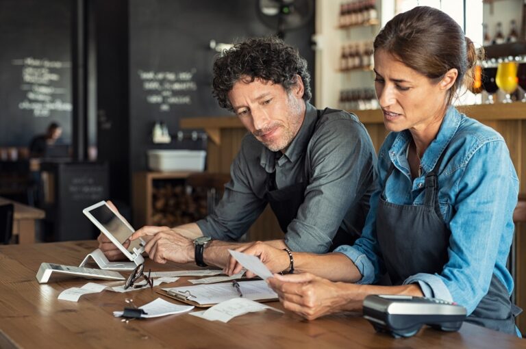 Two Café owners sit at a table checking receipts.