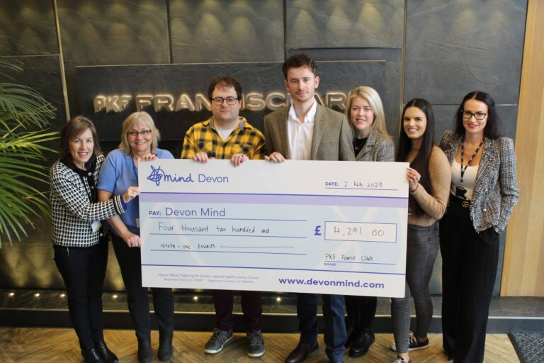 Several colleagues from the Exeter office stand holding a giant cheque, displaying the amount they have raised for Mind Devon.