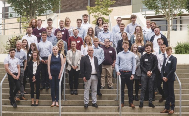 A large group pose on steps while Andrew Richards stands at the front of the group celebrating new trainees.