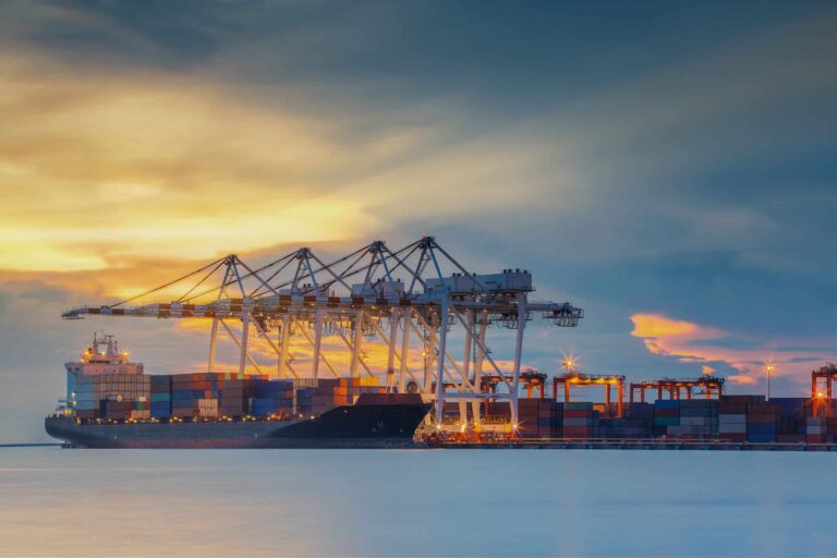 A vessel laden with shipping containers at port as the sun begins to rise.