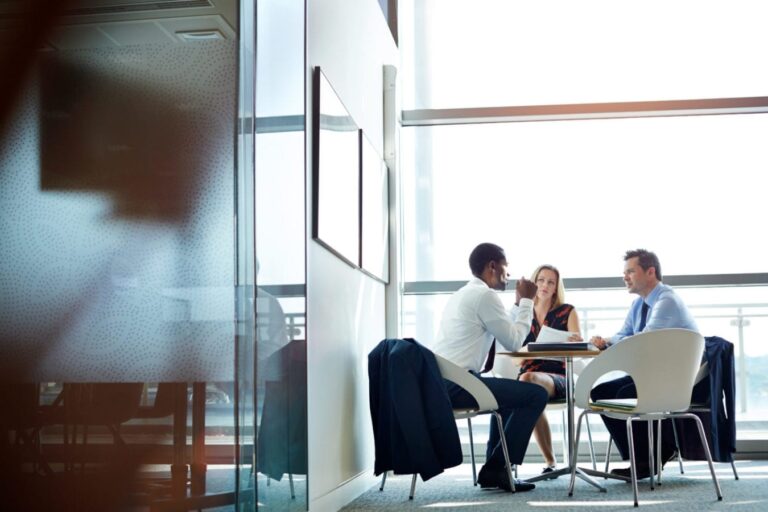 Three people sitting around a table having a meeting in an airy office.