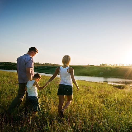 A young family Stoll hand in hand through a field that leads to towards a river.