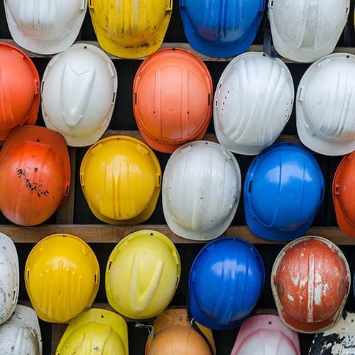 Red, white, yellow, and blue hard hats are hung upon a wall.