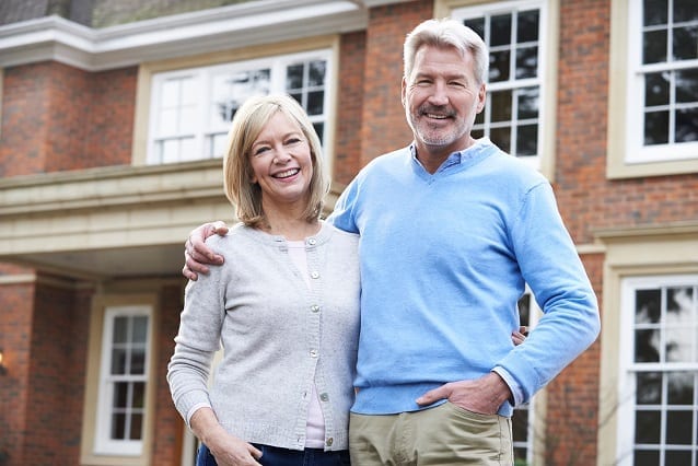 Two property owners stand in front of their house smiling and embracing.