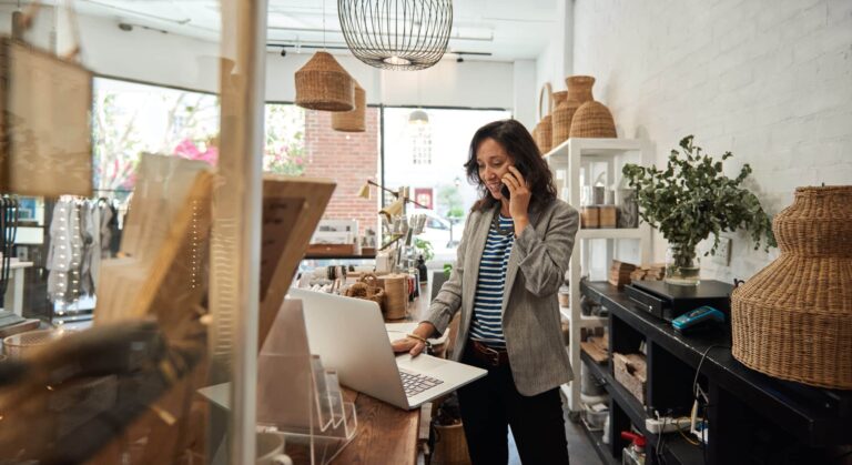 Shop owner looking at laptop whilst talking on a mobile.