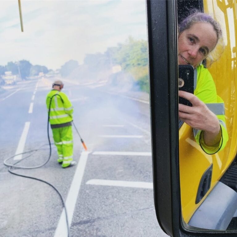 Sinead Kelly-Barber leans out of a truck and snaps a selfie with her smartphone as her co-worker stands behind her, gripping a hose.