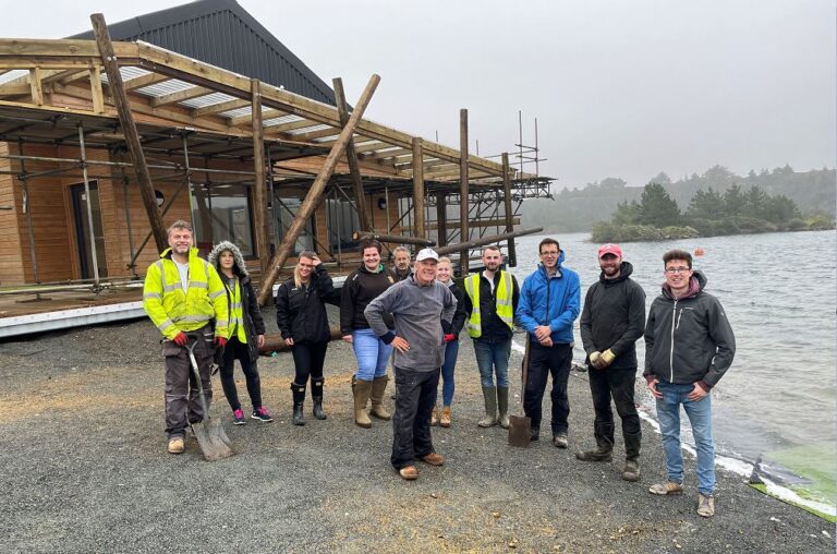 A team of volunteers from the Truro office strikes a pose on the beach, with the new Sailing Centre as their backdrop, under the grey, windswept skies.