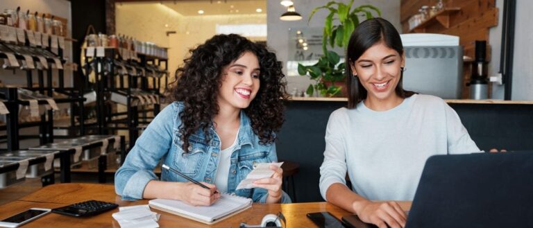 Two female business owners sat at a desk working out their VAT on a laptop computer.