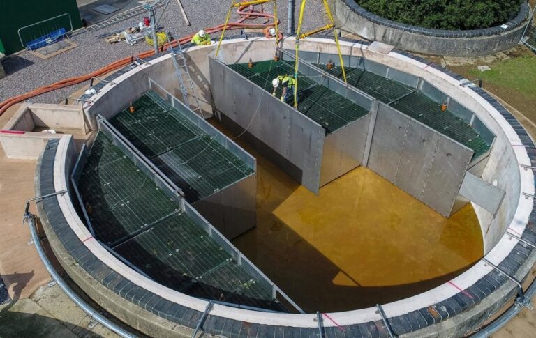 An aerial view of two workers at a wastewater treatment facility, wearing hi-vis clothing and hardhats.