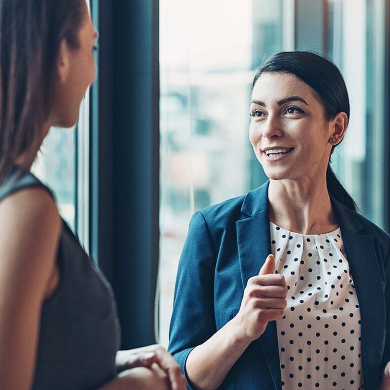 Two female colleagues have a discussion in an office setting.