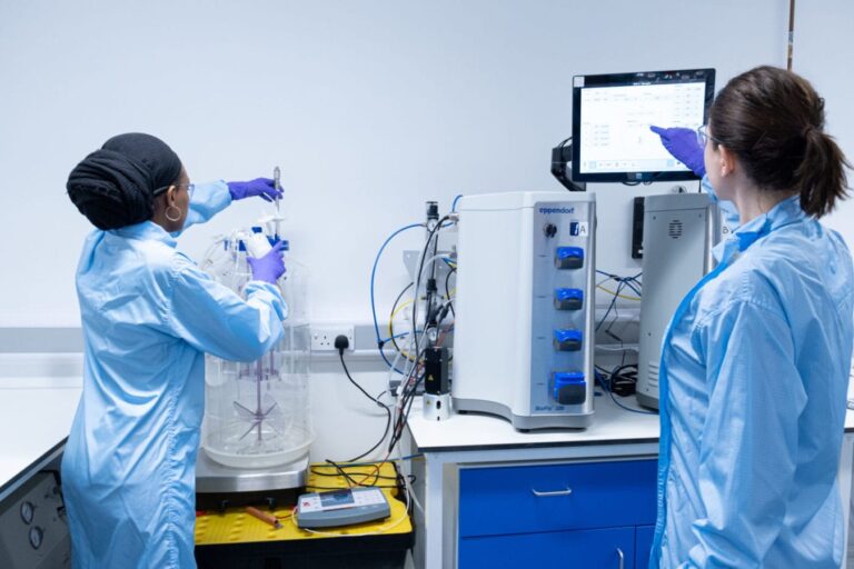 Two ladies are in the eXmoor Pharma laboratory surrounded by equipment with one lady pointing to a computer screen.