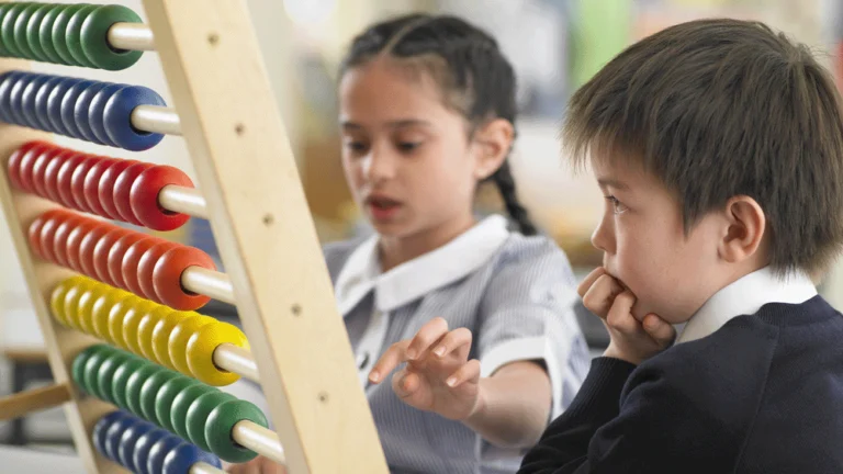 A primary school girl is using a large abacus whilst a boy looks on