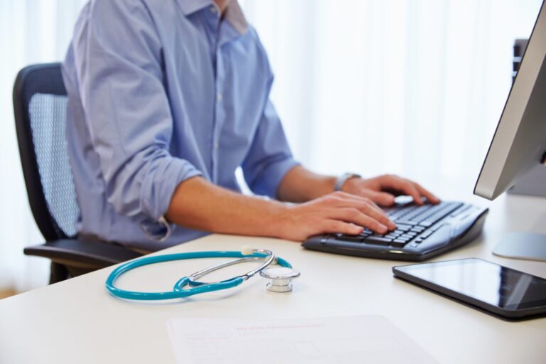 A healthcare professional sits at his desk and enters details into his computer.