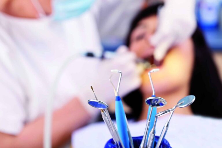 A close up shot of dental equipment in front of the blurred image of a hygienist treating her patient.