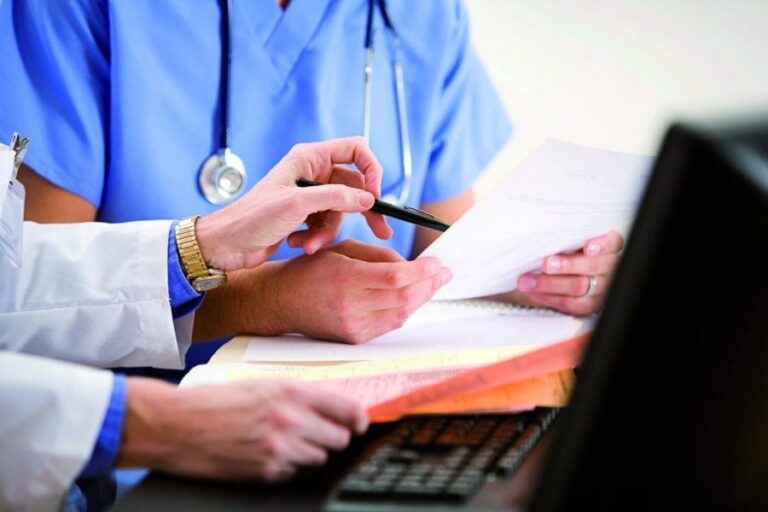 A close up image of the hands and torsos of two healthcare workers discussing records.