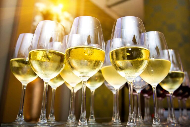 A upward shot of several wine glasses half filled with chilled white wine, lined up on a hotel bar.