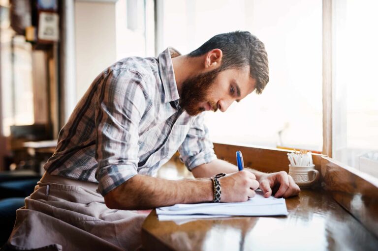 A coffee shop worker fills in paper work while sated at a high bar.