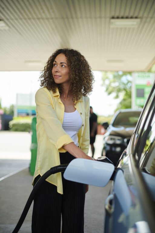 A woman looks at the petrol pump as she holds the nozzle to refuel her car.