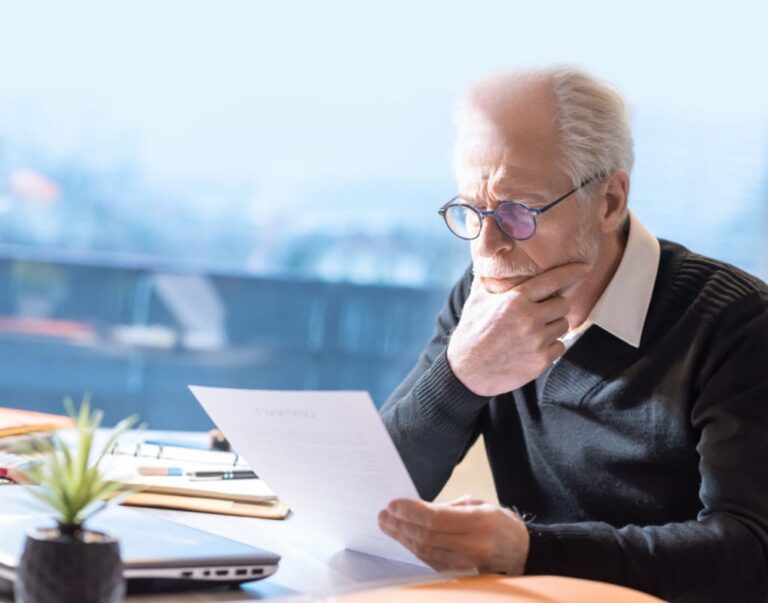 A mature gentleman is seated at a desk, contemplating a legal document.