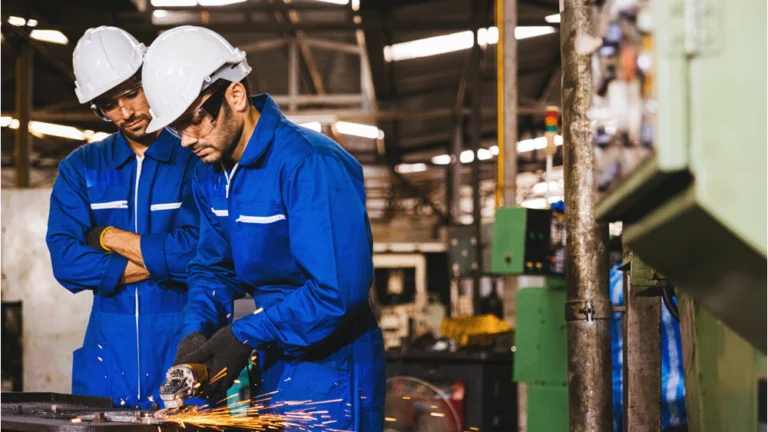 Two men are working in a manufacturing workshop. One is operating equipment that is causing sparks to fly.