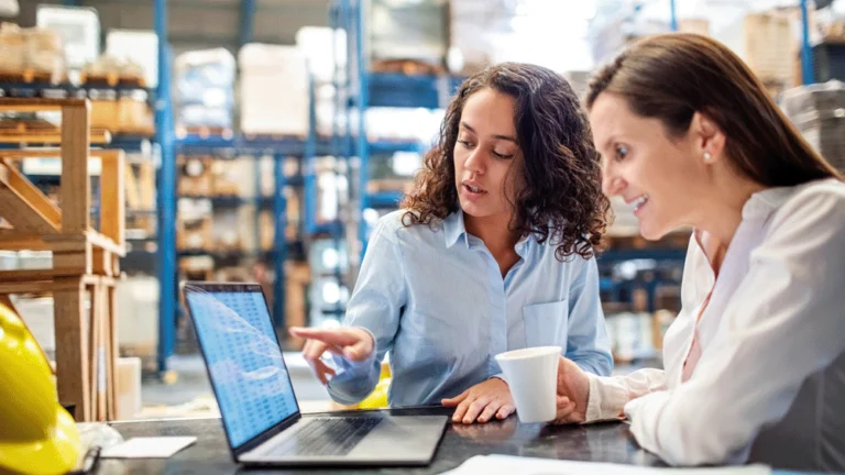 Colleagues discussing payroll figures on computer in warehouse.