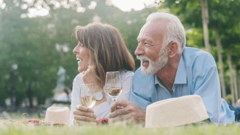 A couple with glasses of wine laying in a field on a summer's day.