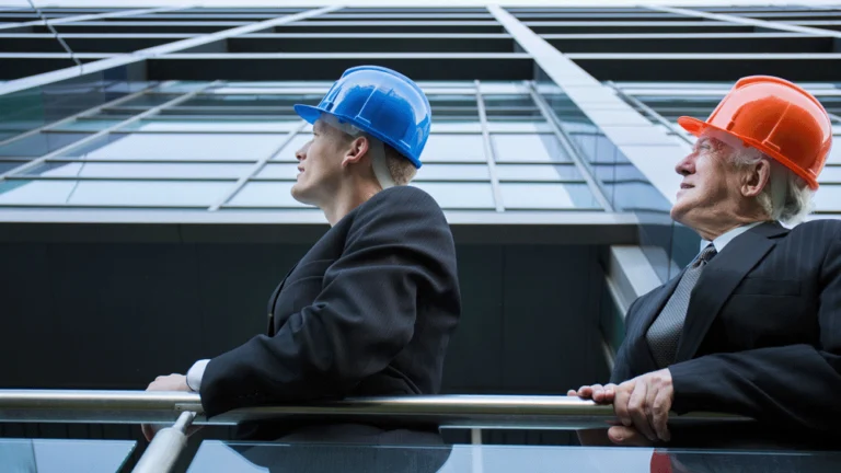 Men in suits with hard hats looking at the outside of a building.