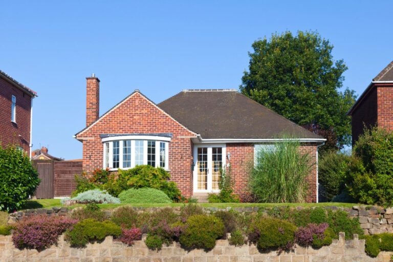 A detached property set against a brilliant blue sky with a vibrant flower bed in the foreground.