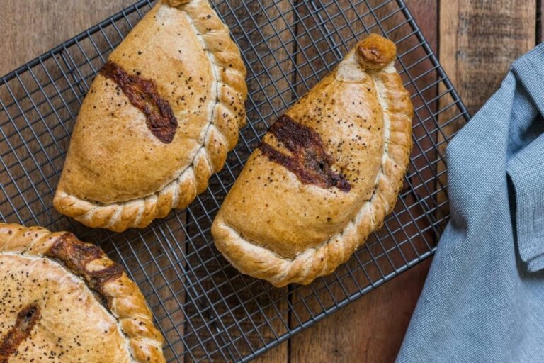 Three hot pasties rest on a cooling tray.