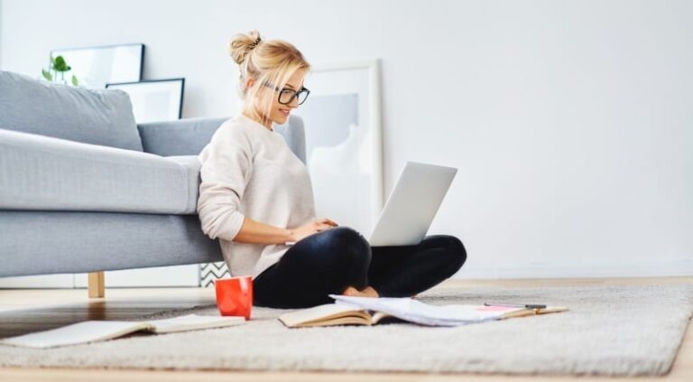 A home worker sits on her living room floor with her lap top computer perched on her knee.