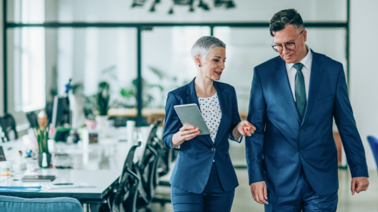 A businessman and businesswoman chatting while walking down an office corridor.