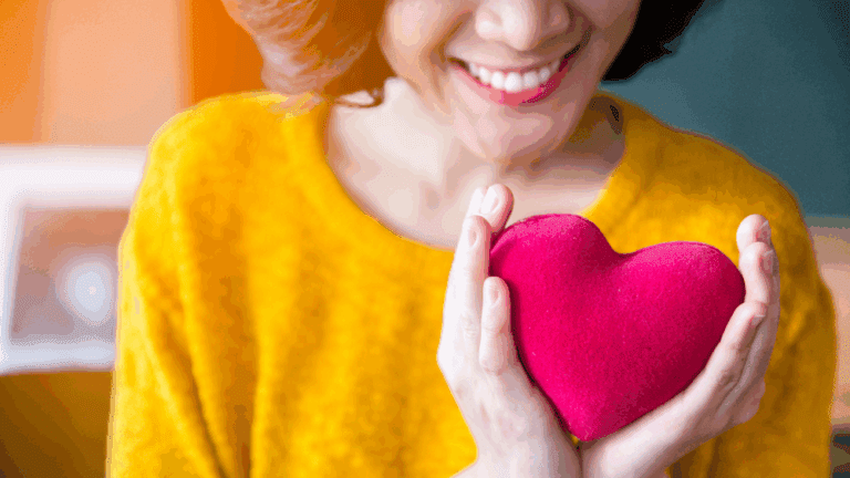 Smiling woman holding a red heart shaped ornament representing charitable giving