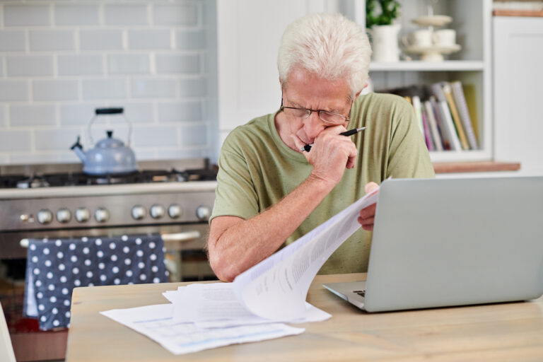 a senior man using a laptop and and going through paperwork at home